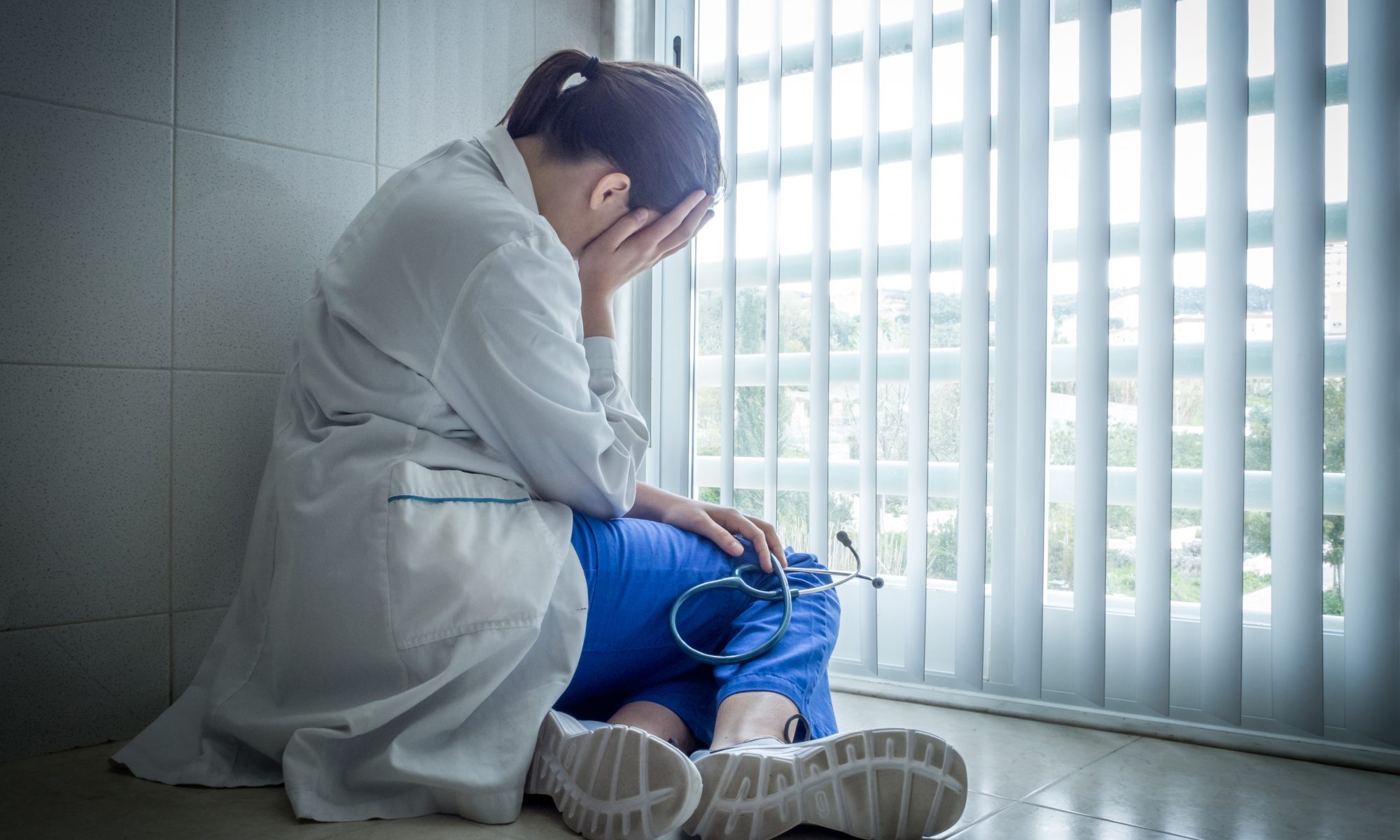 Burnout a depressed young female doctor sitting in despair near a hospital window